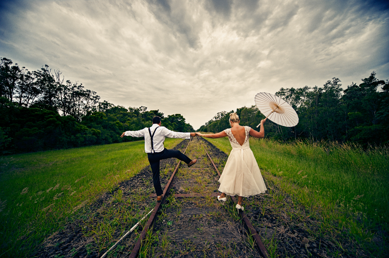 Newlyweds walking hand in hand on a rustic train track